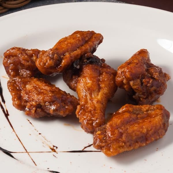 Pizzany's Pizzeria's five glazed chicken wings with a dark sauce drizzle on a white plate.