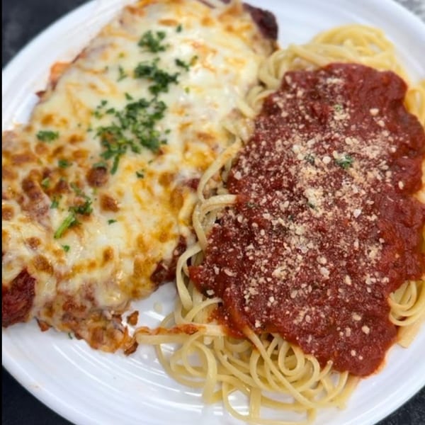 Chicken parmesan with melted cheese and parsley, alongside spaghetti with red sauce and grated cheese.