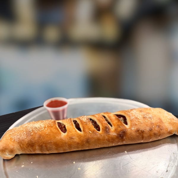 A golden-brown calzone with visible filling through slits, served on a metal tray with a side of marinara.