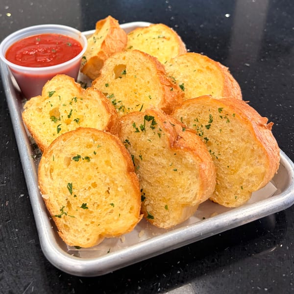 Pizzany's Pizzeria garlic bread with parsley and a side of red marinara sauce on a metal tray.