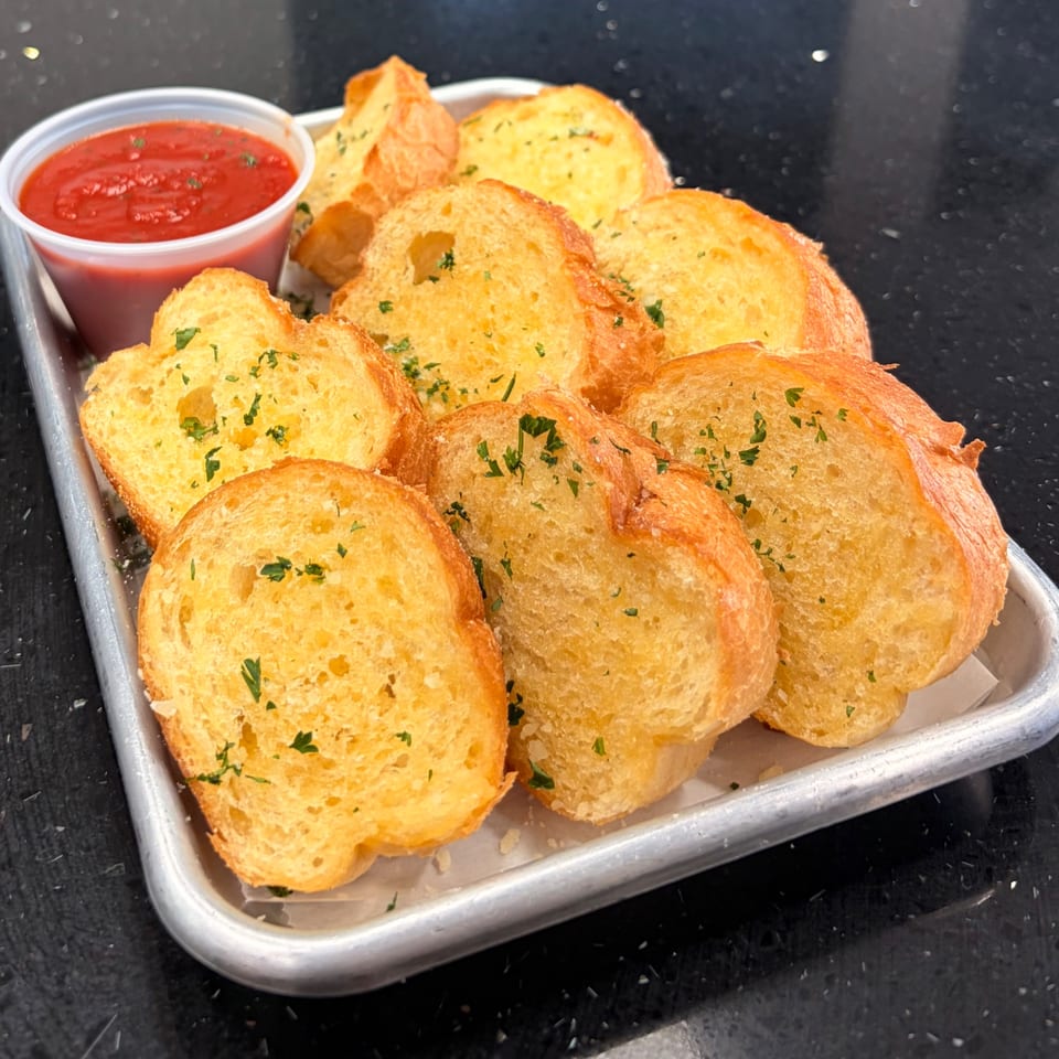 Pizzany's Pizzeria garlic bread with parsley and a side of red marinara sauce on a metal tray.