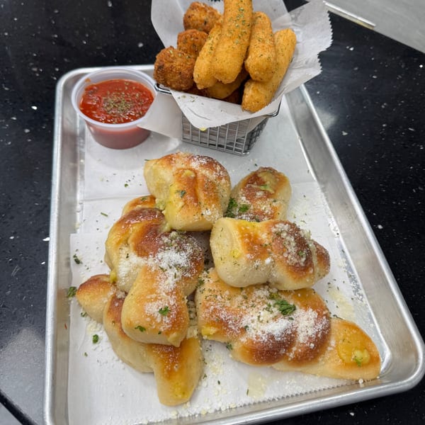 Garlic knots and mozzarella sticks with marinara sauce on a metal tray from Pizzany's Pizzeria.